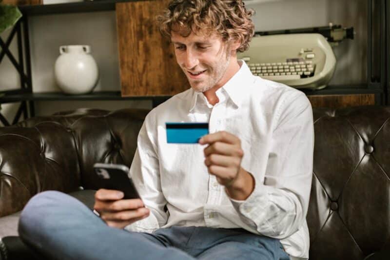 man looking at his cellphone and holding a bank card