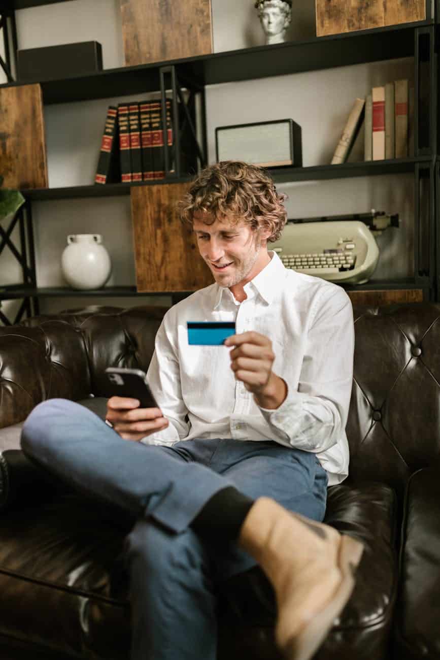 man looking at his cellphone and holding a bank card